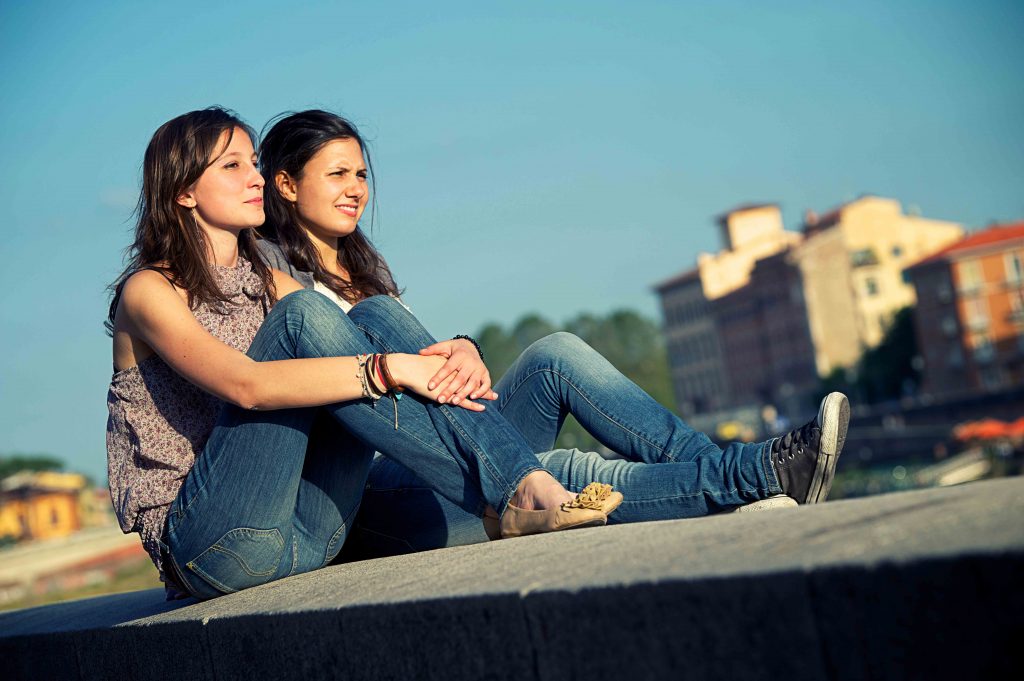 Two female friends sitting on top of a building staring in to the distance