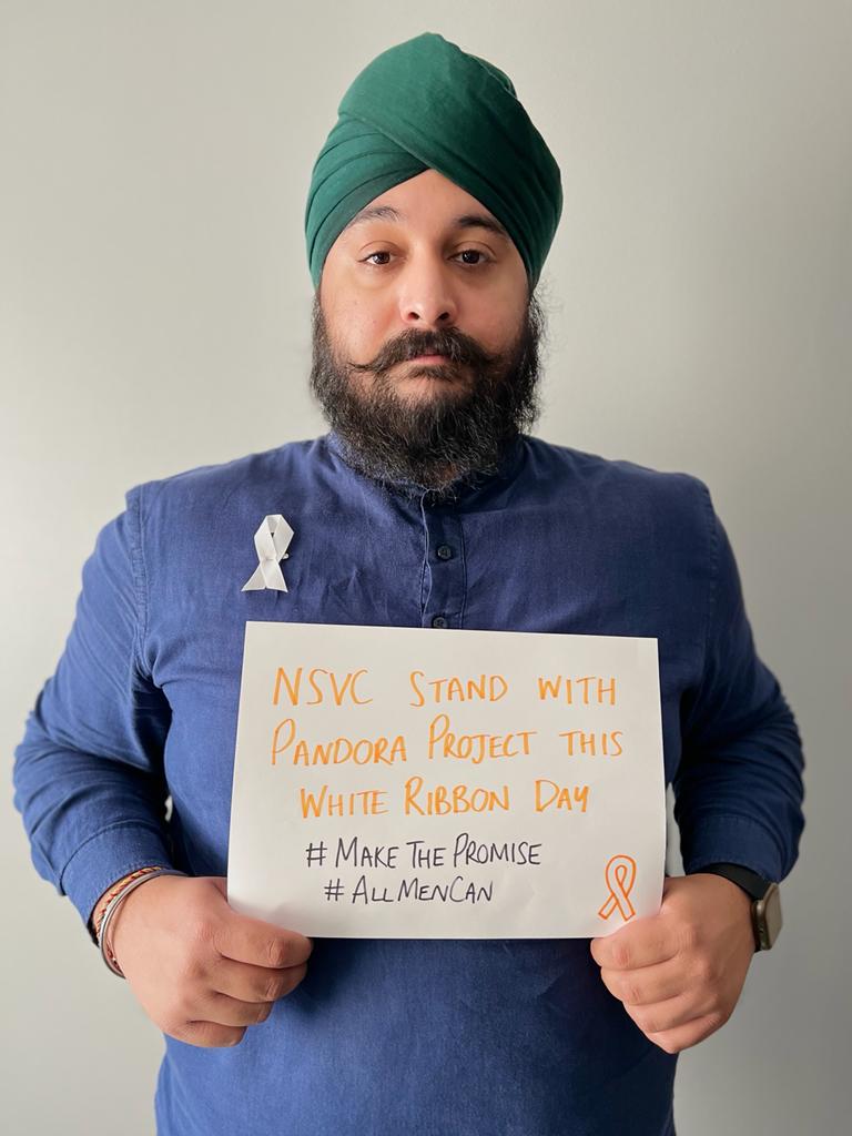 Engagement & Volunteer Officer Anoop holding up a piece of paper reading 'NSVC stand with Pandora Project this White Ribbon Day', alongside the hashtags #AllMenCan and #MakeThePromise